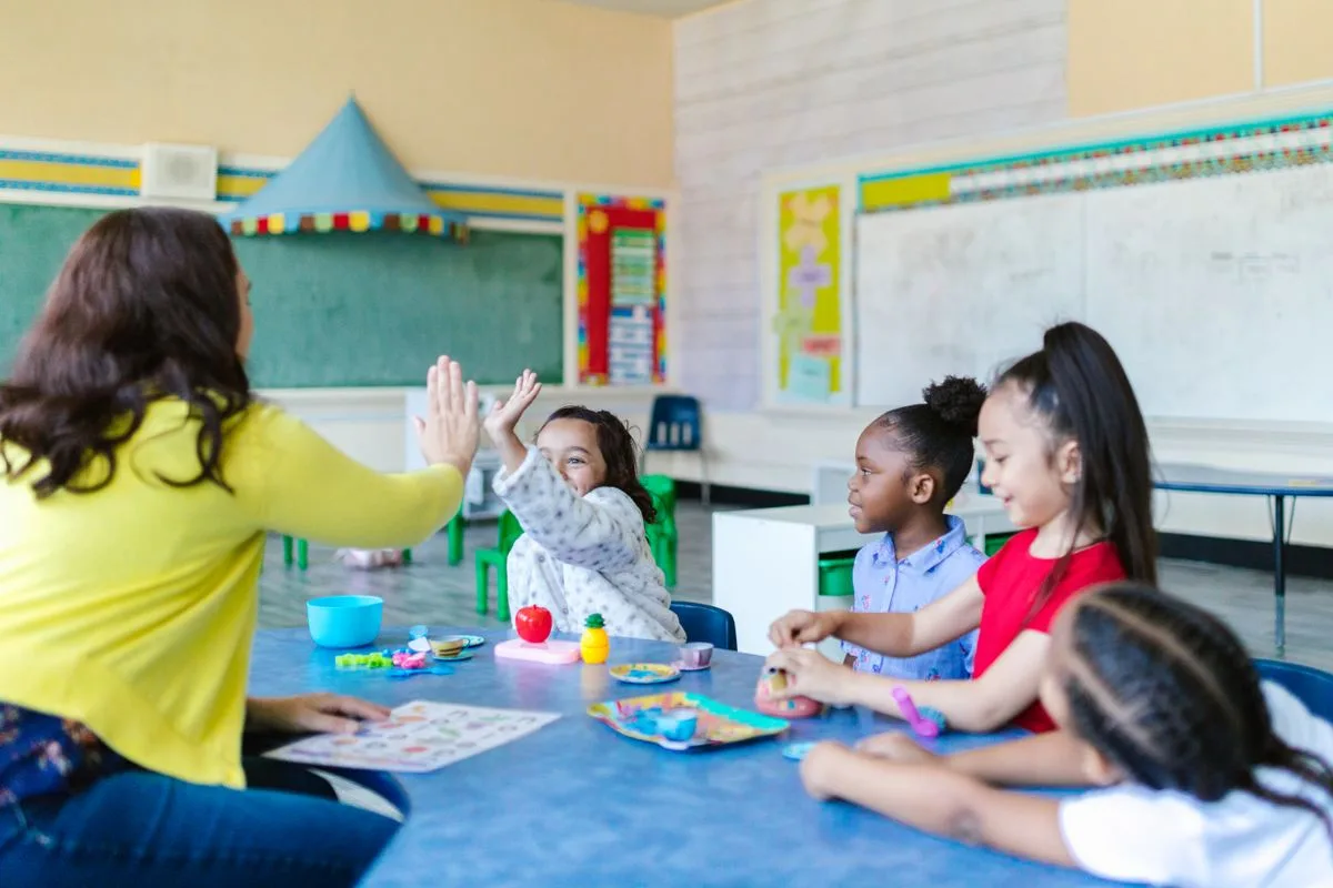 Betreuerin sitzt mit Grundschulkindern am Tisch